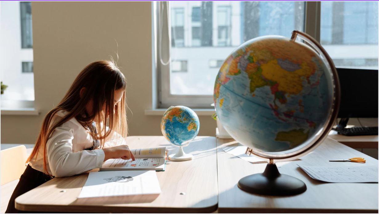 Niña estudiando en el colegio, sobre su mesa dos globos terráqueos