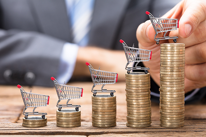 Mano de hombre que construye torres con monedas y en la parte superior mini carro de compra
